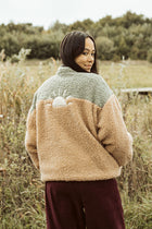 Person wearing a two-tone jacket standing in a field with trees in the background