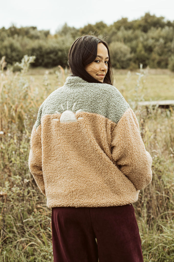 Person wearing a two-tone jacket standing in a field with trees in the background