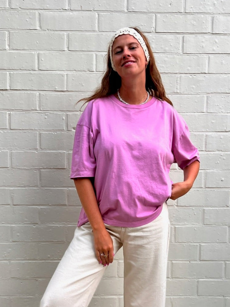 Person wearing a pink t-shirt and white pants standing against a white brick wall.
