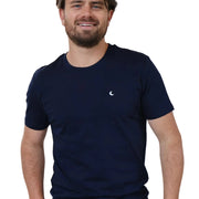 A person wearing a solid blue t-shirt with a subtle white moon embroidery on the chest area, standing in a room with a light fixture behind them.