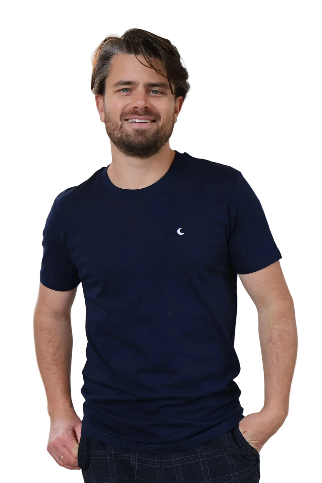 A person wearing a solid blue t-shirt with a subtle white moon embroidery on the chest area, standing in a room with a light fixture behind them.
